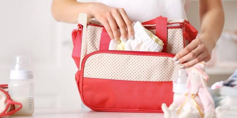 Mother adding spare, clean nappies to a red changing bag