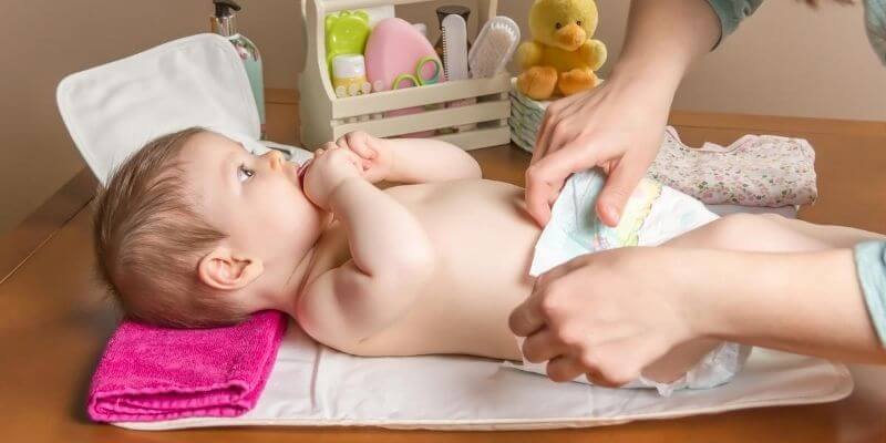 Baby laying on their back on a changing table getting their nappy changed