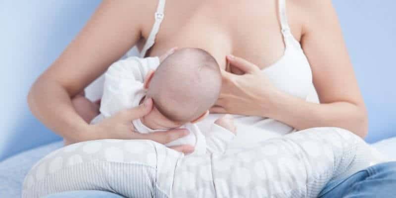 Mother sitting down using a nursing pillow to breastfeed her baby