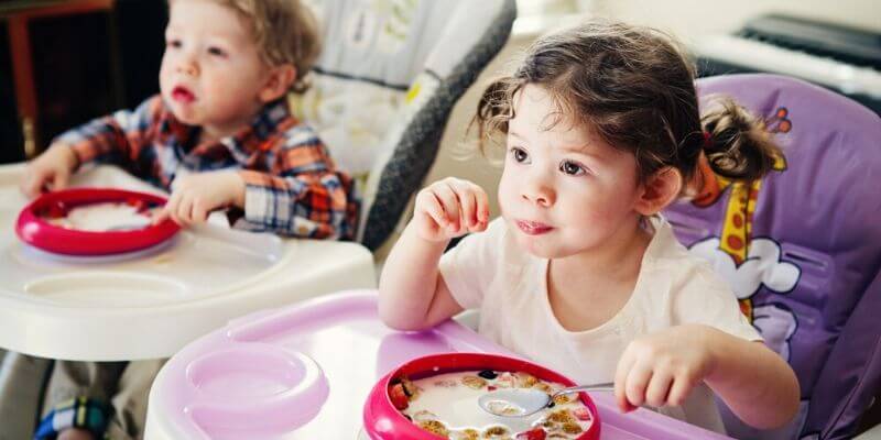 two young children sitting in their high chairs eating